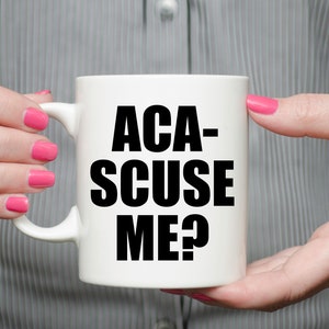 May include: White ceramic mug with black text that reads "ACA-SCUSE ME?"