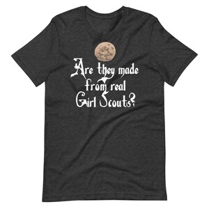 May include: Dark heather grey t-shirt with a white graphic of a moon and the text "Are they made from real Girl Scouts?"