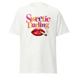 Puede incluir: Camiseta blanca con la frase "Sweetie Darling" en rosa, naranja, morado y amarillo. Debajo, un gráfico de labios rojos con un cigarrillo encendido. El cigarrillo emite una voluta de humo.