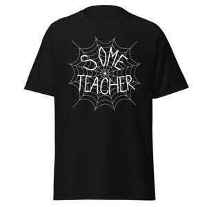 May include: Black t-shirt with a white spiderweb design. The words "SOME TEACHER" are written in white within the web. The shirt is a classic crew neck style.