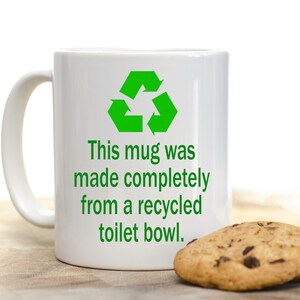 May include: White ceramic mug with a green recycling symbol and the text "This mug was made completely from a recycled toilet bowl."