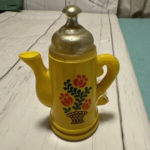 May include: Yellow ceramic teapot with a silver lid and a floral design. The teapot has a handle and a spout.