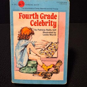 May include: A Dell Yearling Book cover featuring a girl sitting on a stool and drawing on a large pad of paper. The book title is "Fourth Grade Celebrity" by Patricia Reilly Giff, illustrated by Leslie Morrill.