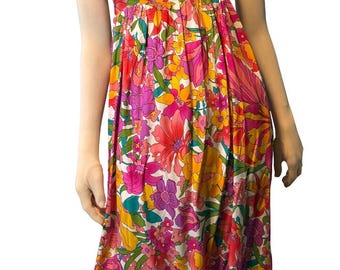 May include: A colorful floral print dress with a square neckline and short, puffed sleeves. The dress features a vibrant pattern of pink, yellow, and purple flowers on a white background. The dress has a flowing, tiered skirt.