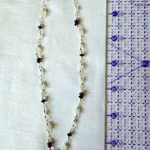 May include: A silver chain necklace with white and red gemstone beads. The necklace has a toggle clasp.
