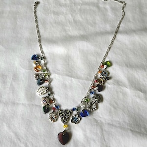 May include: Silver-toned necklace with a variety of charms, including hearts, flowers, and beads in multiple colors. The necklace has a delicate chain and a lobster claw clasp. The charms are made of metal and colorful glass.
