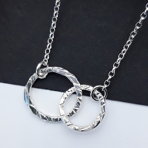 May include: A silver necklace featuring two interlocked circles. The circles have a textured finish and are joined by a fine chain.