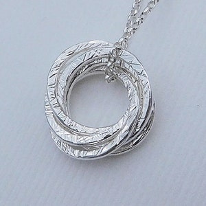 May include: Silver necklace with a pendant made of five interlocking rings. The rings are textured and have a polished finish.