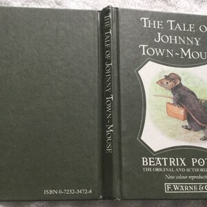 Puede incluir: Un libro de tapa dura verde con el título "The Tale of Johnny Town-Mouse" de Beatrix Potter. El libro presenta una ilustración a color de un ratón con un sombrero y llevando una maleta.