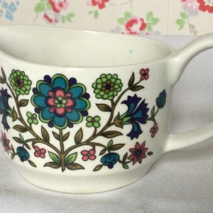 May include: White ceramic gravy boat with a floral pattern in shades of blue, green, pink, and brown. The floral design features stylised flowers and leaves.