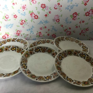 May include: Set of six white ceramic dinner plates with a brown, orange, and yellow floral pattern around the rim.