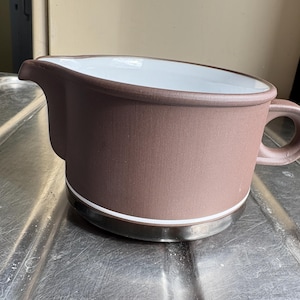 Könnte beinhalten: Ein brauner Keramik-Milchkännchen mit weißem Innenraum und einem weißen Band um den oberen Rand. Der Milchkännchen hat einen Griff und eine abgerundete Form.