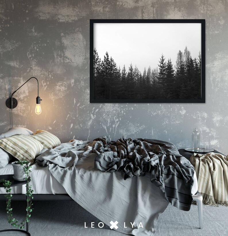 May include: A black and white photograph of a forest with tall trees, framed in a black frame, hangs on a grey wall above a bed with a grey and white striped throw blanket and a grey duvet cover.