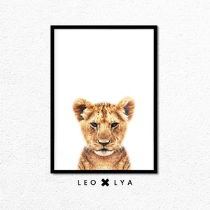 May include: A close-up portrait of a lion cub with a white background. The cub has a light brown coat and a serious expression. The text "LEO x LY A" is printed below the image.