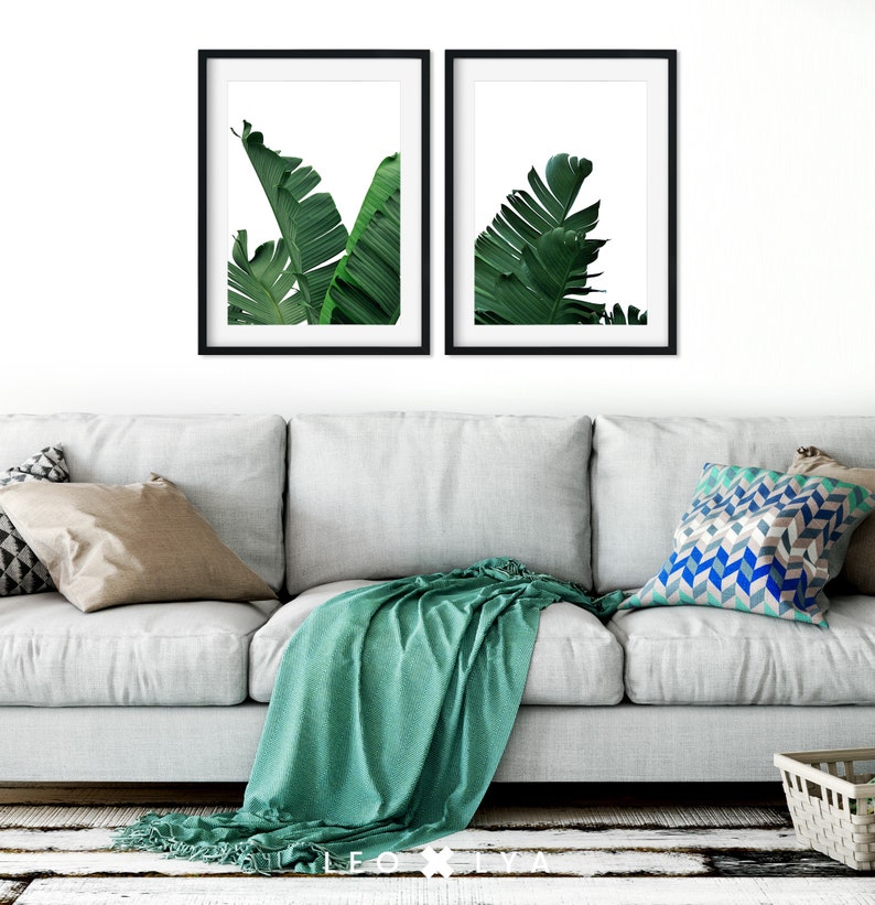 Puede incluir: Dos impresiones enmarcadas de hojas verdes de pl&aacute;tano sobre un fondo blanco. Las impresiones est&aacute;n colgadas en una pared blanca sobre un sof&aacute; gris claro con una manta verde y almohadas.
