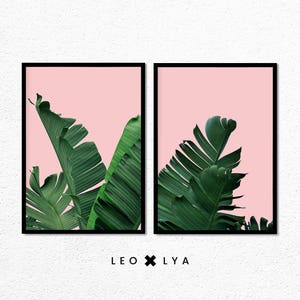 May include: Two framed prints with a pink background and green banana leaves. The prints are side-by-side and have black frames. The text "LEO x LY A" is below the prints.