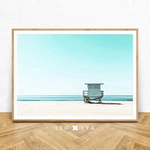 K&ouml;nnte beinhalten: Ein gerahmtes Foto eines Rettungsschwimmers auf einem Strand mit blauem Himmel und Meer im Hintergrund. Der Rettungsschwimmerstand tr&auml;gt die Nummer "117".