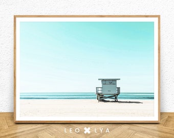 May include: A framed photograph of a lifeguard stand on a beach with a blue sky and ocean in the background. The lifeguard stand has the number "117" on it.