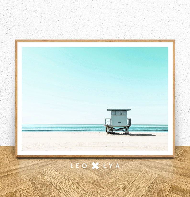 K&ouml;nnte beinhalten: Ein gerahmtes Foto eines Rettungsschwimmers auf einem Strand mit blauem Himmel und Meer im Hintergrund. Der Rettungsschwimmerstand tr&auml;gt die Nummer "117".