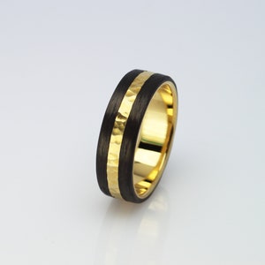May include: A black carbon fiber ring with a gold band. The gold band has a hammered texture.