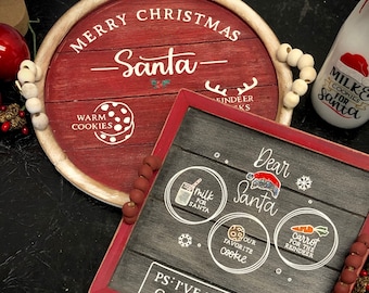 Può includere: Un vassoio di legno rosso con lettere bianche che dicono "Buon Natale - Babbo Natale -" e "Biscotti caldi". Il vassoio ha perline bianche attorno al bordo. Una lavagna nera con cornice rossa dice "Caro Babbo Natale" e ha tre cerchi con illustrazioni di un bicchiere di latte, un biscotto e una carota. La lavagna dice anche "PS: Sono stato molto buono quest'anno".
