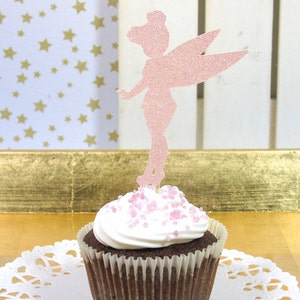 Puede incluir: Topper de cupcake de hada de purpurina rosa sobre un cupcake de chocolate con glaseado blanco y chispas rosas.