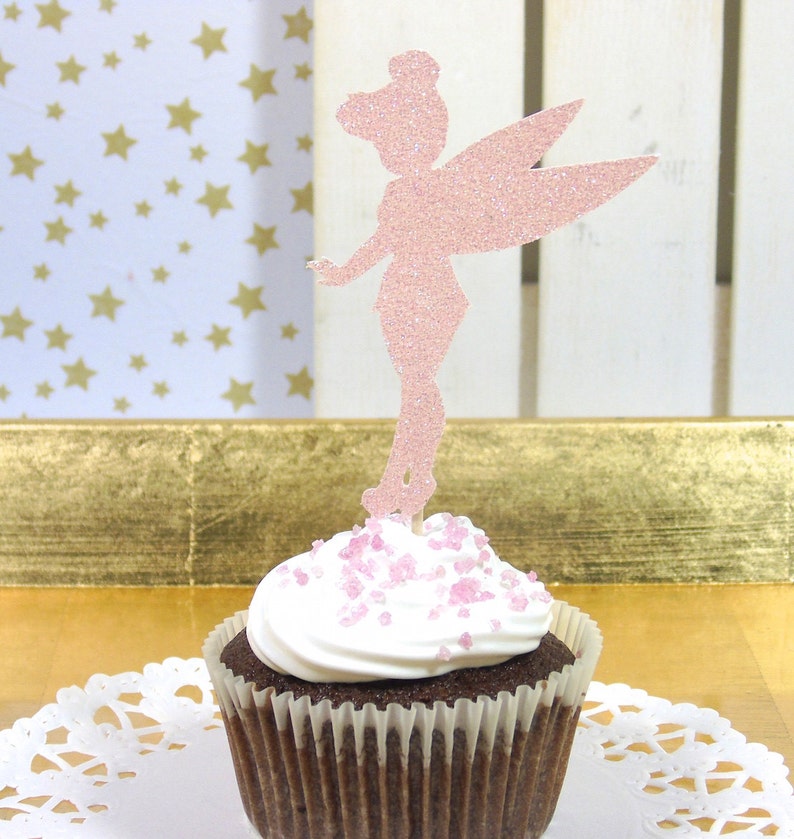 Puede incluir: Topper de cupcake de hada de purpurina rosa sobre un cupcake de chocolate con glaseado blanco y chispas rosas.