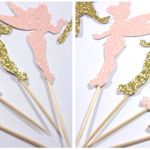 Puede incluir: Un conjunto de diez adornos para cupcakes con siluetas de hadas de purpurina rosa y dorada. Las hadas est&aacute;n en varias poses de vuelo con las alas extendidas. Los adornos est&aacute;n unidos a brochetas de madera.