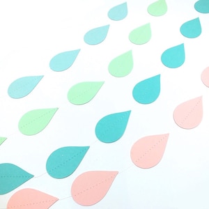 Peut inclure: Une guirlande de gouttes de pluie en papier pastel dans des tons de rose, vert et bleu. Les gouttes de pluie sont enfilées sur un fil blanc.