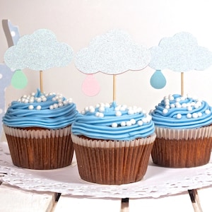 May include: Three blue cupcakes with white frosting and pearl sprinkles topped with cloud-shaped toppers with raindrops. The cupcakes are on a white doily.