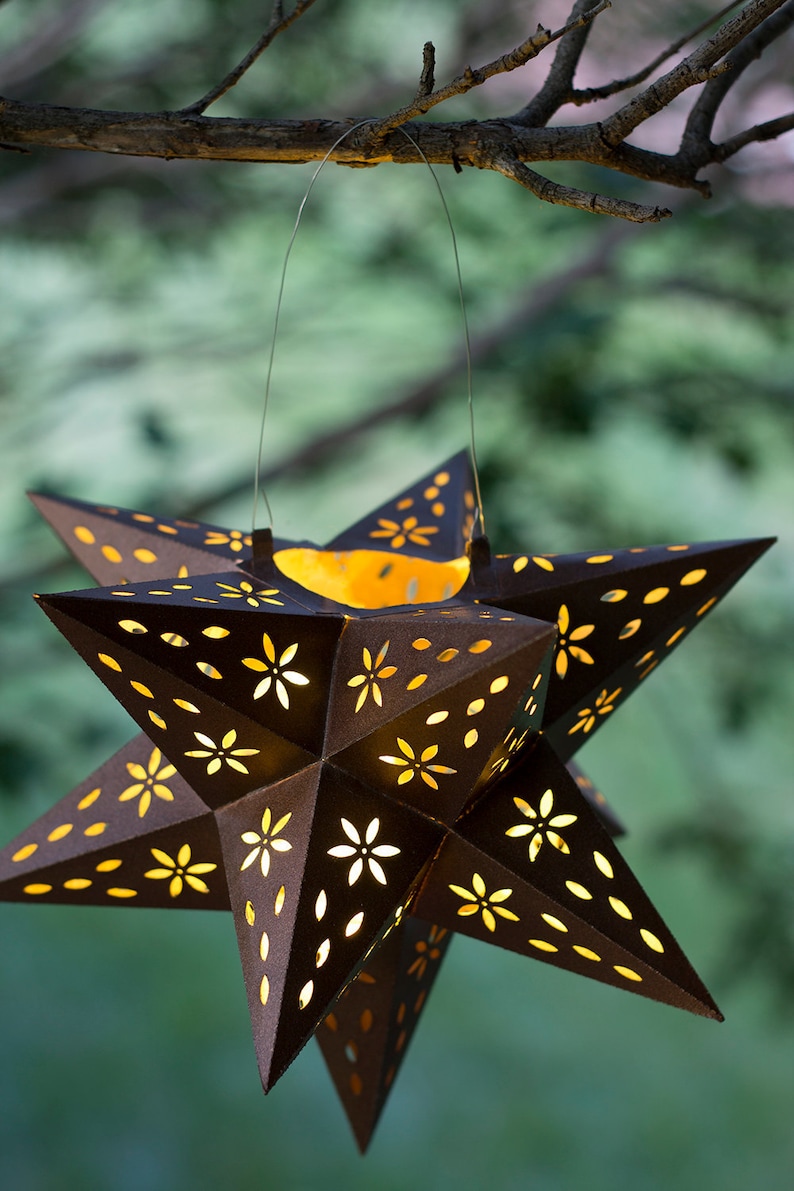 May include: A brown metal star-shaped lantern with cut-out floral designs. The lantern is lit from within, casting a warm glow.