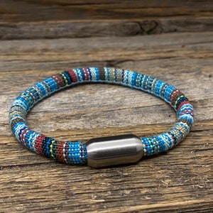May include: A colorful woven bracelet with a silver magnetic clasp. The bracelet is made of a variety of colors, including blue, green, red, and white.