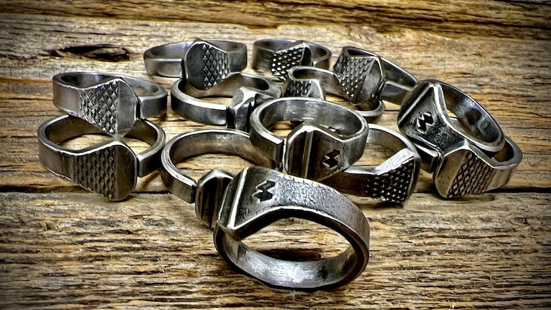 May include: A group of silver metal rings, each made from a horseshoe nail. The rings are stacked on top of each other and have a textured surface.