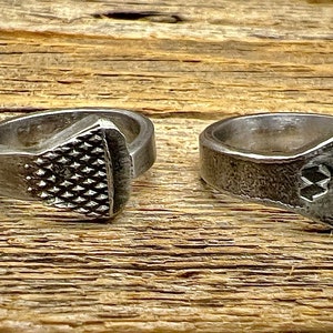 May include: Two silver metal rings made from repurposed horseshoe nails. One ring has a textured, diamond-shaped design on the top. The other ring has a simple, flat top.