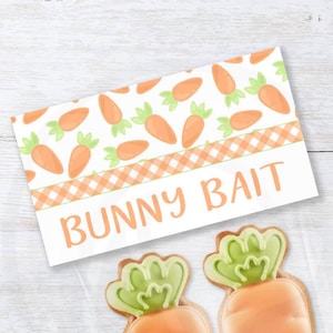 Könnte beinhalten: Druckbarer Oster-Süßigkeitentaschen-Topper mit Karottenmuster und dem Text "Bunny Bait". Zwei karottenförmige Kekse sind im Bild enthalten.