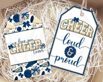 Puede incluir: Dos etiquetas de regalo con un tema de porra. Una etiqueta tiene un diseño de porra azul y dorado con el texto "We love our cheer team". La otra etiqueta tiene un fondo blanco con texto azul y dorado que dice "Cheer loud & proud".