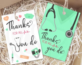 May include: Two gift tags with medical-themed illustrations. One tag is white with a stethoscope, syringe, and the text "Thanks for all you do." The other tag is light green with a stethoscope and the same text. Both tags have a brown string attached.