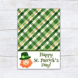 以下が含まれることがあります： 上部に緑のチェック柄のデザインが施された、聖パトリックの日のグリーティングカード。下部にはレプラコーンのイラストと「Happy St. Patrick's Day！」の文字が装飾的なフォントで描かれています。カードの背景は白です。