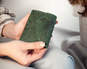 May include: A green leather wallet with an intricate embossed pattern. The wallet is folded in half and held in a person's hand.