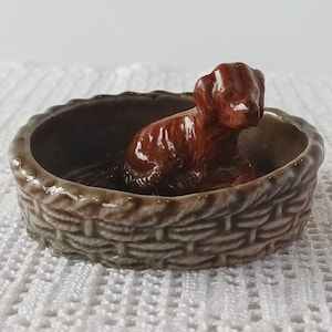 Peut inclure: Une figurine de chien en céramique brune assise dans un panier pour chien en céramique brun et blanc.