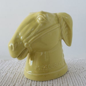 May include: A yellow ceramic horse head money box with the words "Missouri Mule" on the base.