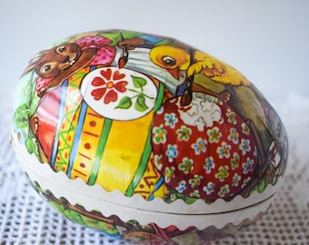 May include: A vintage Easter egg-shaped candy box with a colourful illustration of a bunny, a chick, and flowers. The box is made of cardboard and has a scalloped edge.
