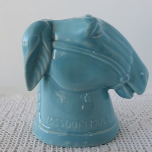 May include: A light blue ceramic horse head figurine with the words "Missouri Mule" on the bottom.