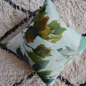 May include: A light blue throw pillow with a watercolor-style floral pattern in shades of green, brown, and white.