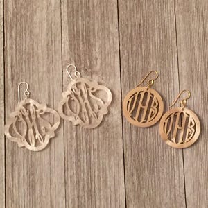 May include: Two pairs of monogram earrings. One pair is gold with a round design and the other pair is silver with a more intricate design. Both pairs feature the monogram "VHB".