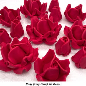 Può includere: Una collezione di rose 3D color rubino, alcune completamente sbocciate e altre in bocciolo, sono sparse su una superficie bianca. Le rose presentano petali dettagliati e una consistenza vellutata. Il testo "Ruby (Very Dark) 3D Roses" è in basso.