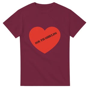 May include: Burgundy t-shirt with a large red heart design. The heart has the words "SOUTH SHIELDS" printed across it in black. The t-shirt is a solid colour and has short sleeves.