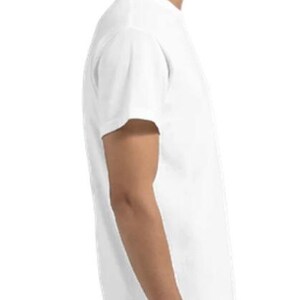 May include: A plain white t-shirt with short sleeves. The shirt is made of a soft material and is being worn by a person. The person is wearing blue jeans. The shirt is a basic, versatile garment.