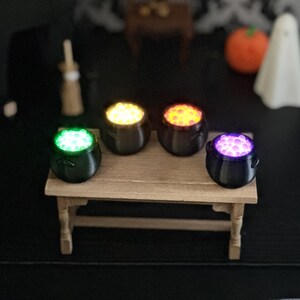 An elevated view of the four glowing miniature cauldrons arranged on a wooden miniature table in front of a Halloween diorama backdrop.