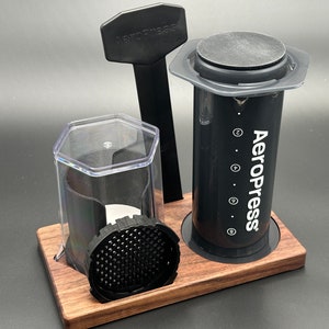 May include: A black AeroPress coffee maker with a wooden base and a clear plastic container. The AeroPress is a popular method for brewing coffee at home.